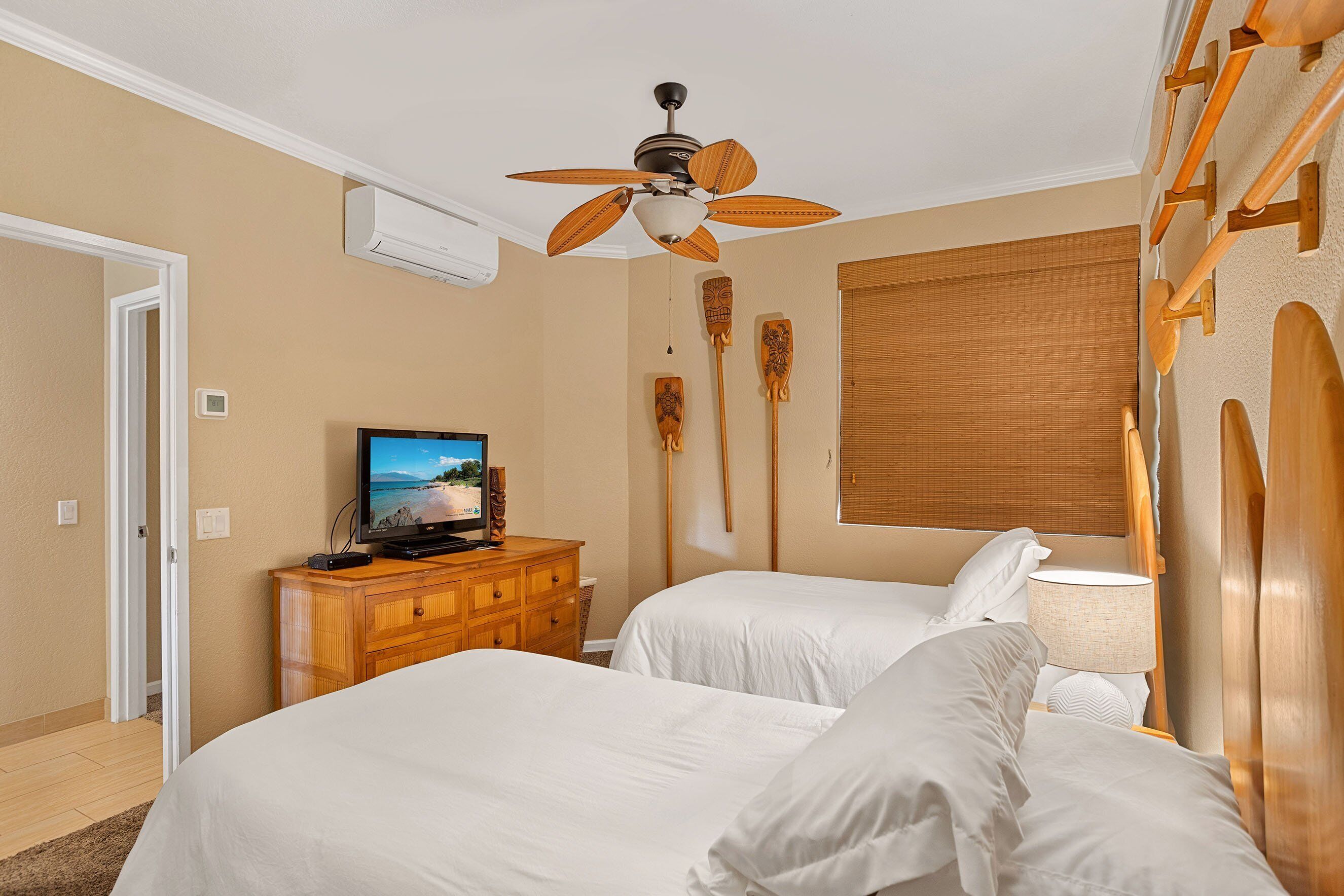 A hotel room with two beds, a ceiling fan, a television, wooden headboards, and a window with blinds.