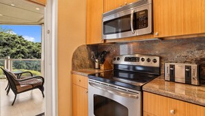 Una cocina con gabinetes de madera, un microondas de acero inoxidable, una estufa y un tostador.