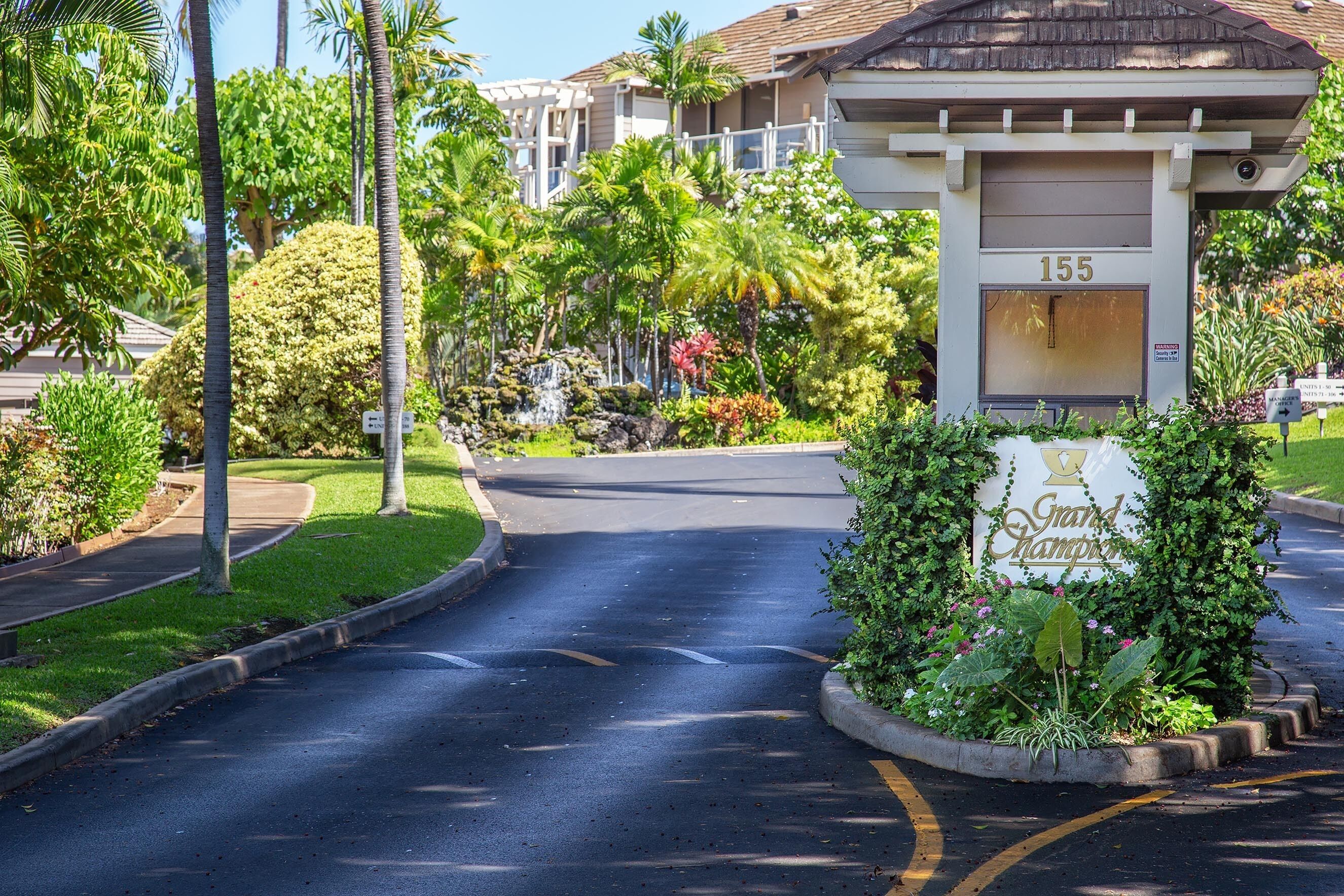 A gated entrance with a sign reading "Grand Champion" and the number 155, surrounded by lush greenery and palm trees.