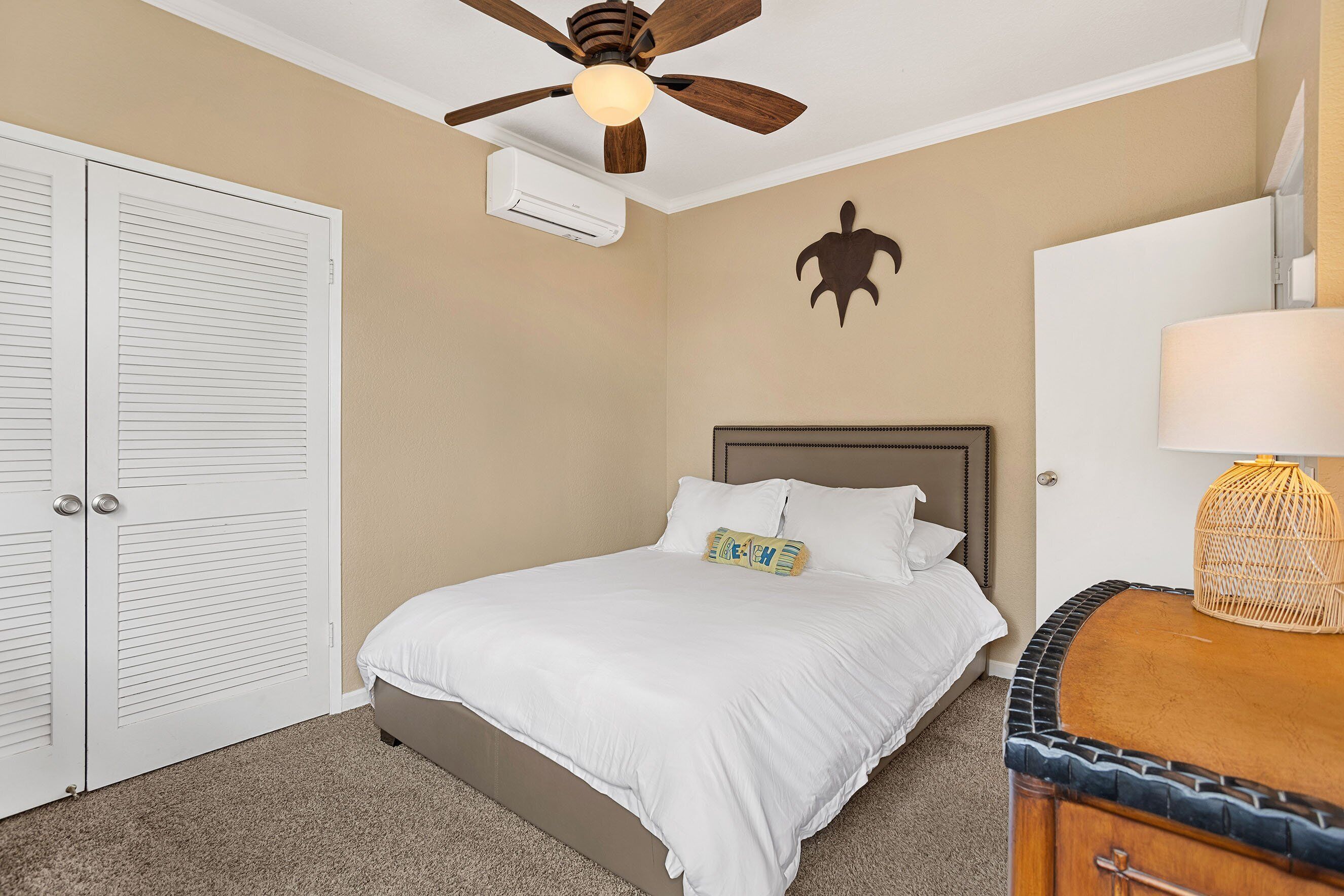 Una camera da letto con un letto, una ventola a soffitto, un condizionatore d'aria, una decorazione a parete, un comodino con una lampada e un armadio in legno.
