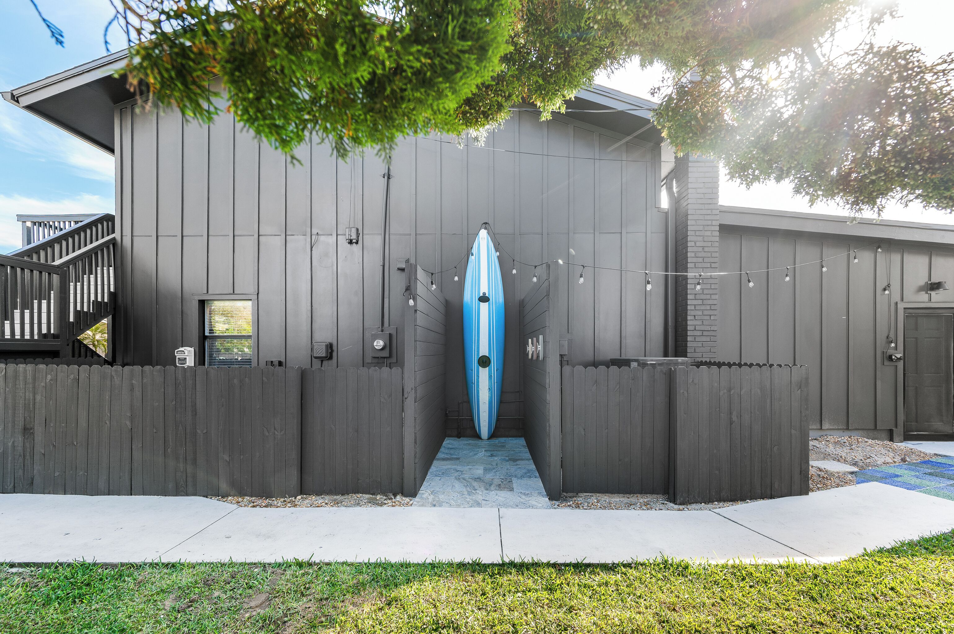 A modern building with a wooden fence, a blue surfboard, and string lights.