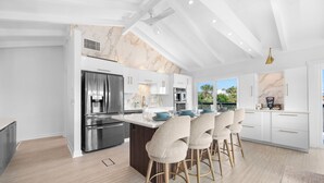 A modern kitchen with marble backsplash, stainless steel appliances, and a bar area with stools. - Private Pool/Spa! 4 Min Walk to Vilano Beach. Two Living Rooms & Kitchens (St. Augustine)