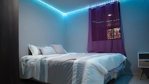 A bedroom with a bed, a nightstand, and a window with purple curtains.