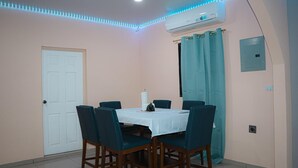 Un coin repas avec une table dressée pour six personnes, entourée de chaises, d’un appareil de climatisation et d’une porte.