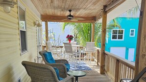 A covered porch with wicker furniture, a small table, and a grill. - Beautiful house on Sunset Beach in Treasure Island with outdoor balcony. (Treasure Island)