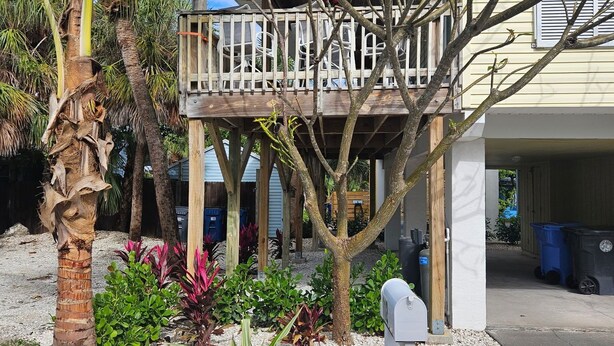 A house with a wooden deck, surrounded by a garden with various plants and a palm tree. - Beautiful house on Sunset Beach in Treasure Island with outdoor balcony. (Treasure Island)