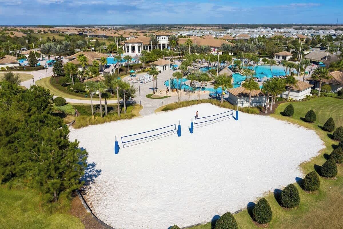 An aerial view of a resort with multiple swimming pools, a tennis court, and a large white sand area.