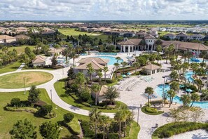 A residential area with a central swimming pool, multiple lounge areas, and a golf course in the background. - 6-Bedroom Single House in Champions Gate (Four Corners)