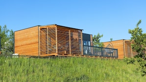 Une cabane moderne en bois, avec un revêtement extérieur à lattes, un balcon et un ciel bleu clair en arrière-plan.