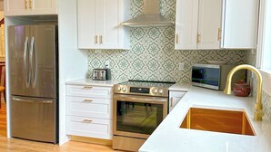 A kitchen with white cabinets, a stainless steel refrigerator, an oven, a microwave, and a sink with a gold faucet. - Beautifully restored 4-bdr w/ 4 ensuites. G&J on Queen's located downtown! (St. John's)
