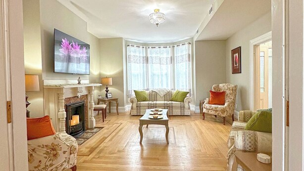 A living room with a fireplace, a television mounted on the wall, and a large window with curtains. - Beautifully restored 4-bdr w/ 4 ensuites. G&J on Queen's located downtown! (St. John's)