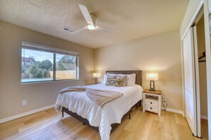Un dormitorio con una cama, dos mesitas de noche con lámparas, un ventilador de techo, una ventana y una puerta.