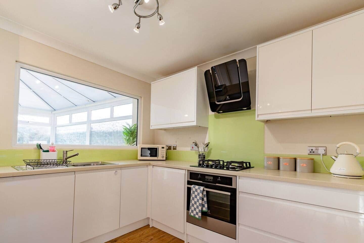 Una cocina moderna con armarios blancos, microondas, estufa a gas y ventana con vistas a zonas verdes.