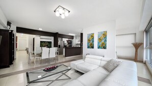 A modern living room with a white sofa, a glass coffee table, and a dining area with white chairs. - YC 1701l Apartamento 2 BDR Av Balboa (Panama City)