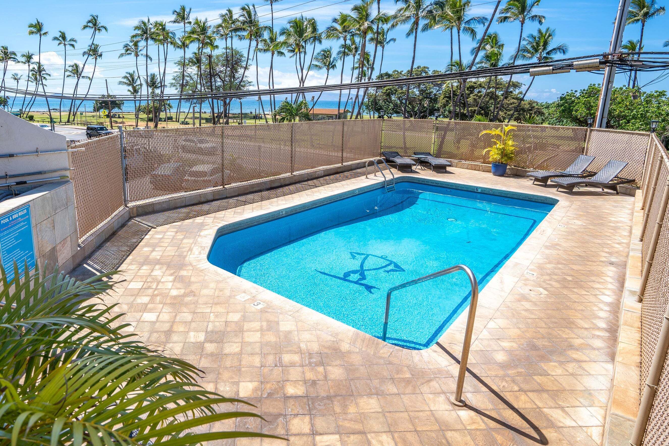 Una piscina rectangular con revestimiento azul, rodeada por una solana con baldosas y una valla.