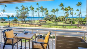 A balcony with a view of the ocean and palm trees, a table with chairs, and a railing. - Island Surf 304 - Modern Renovation, Must See Ocean View, Cool Split AC, Wi-fi ! (Kihei)