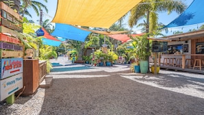 A courtyard with a gravel path, palm trees, and various signs indicating amenities like a restaurant, parking, and a bird stand. - Island Surf 304 - Modern Renovation, Must See Ocean View, Cool Split AC, Wi-fi ! (Kihei)