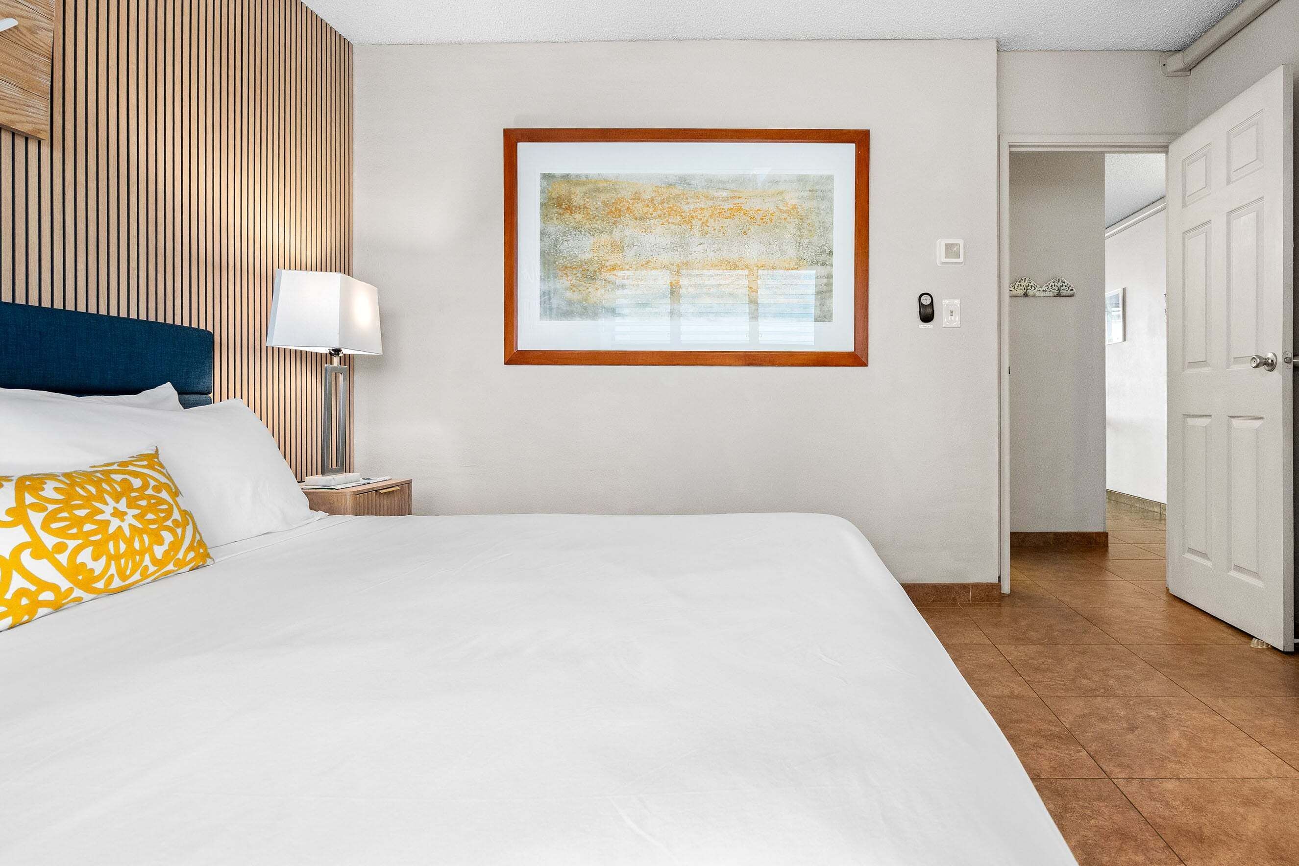 A hotel room with a large bed, a nightstand, a lamp, and a framed artwork on the wall.