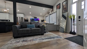 A modern living room with a grey sofa, a TV, and a kitchen in the background.