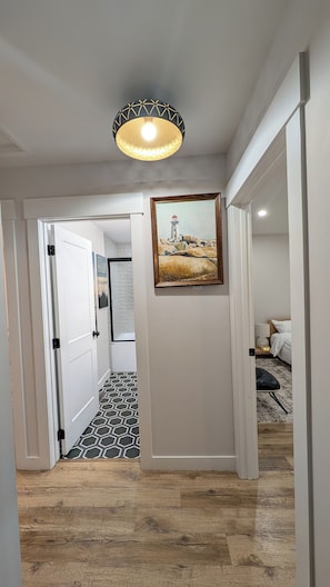A hallway with a patterned floor, a painting of a lighthouse, and a ceiling light fixture.