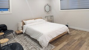 Un dormitorio con cama, ventilador de techo, espejo redondo, pequeña mesa, silla y ventana con persianas.