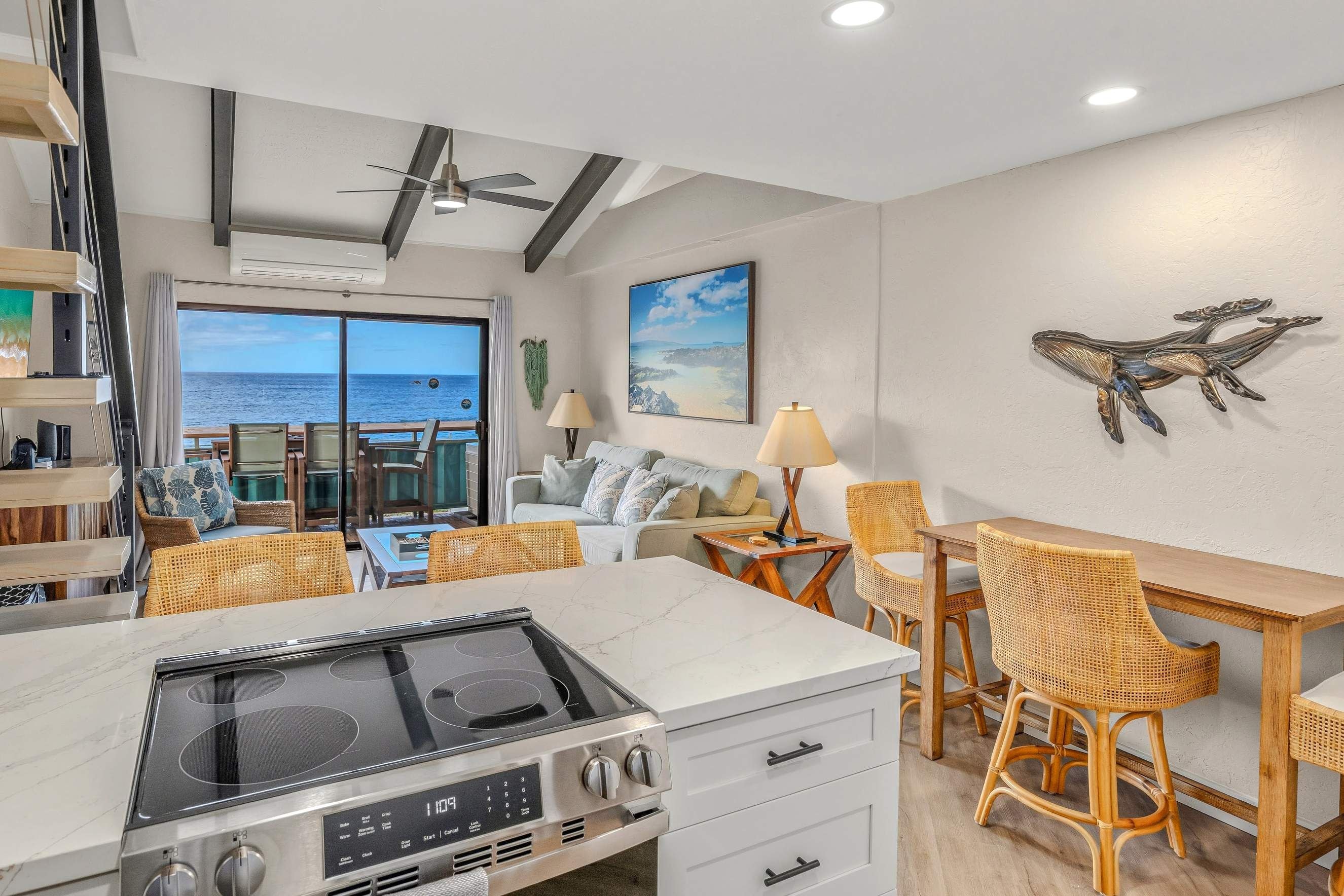 A modern kitchen with a view of the ocean, wicker furniture, and a dining area.