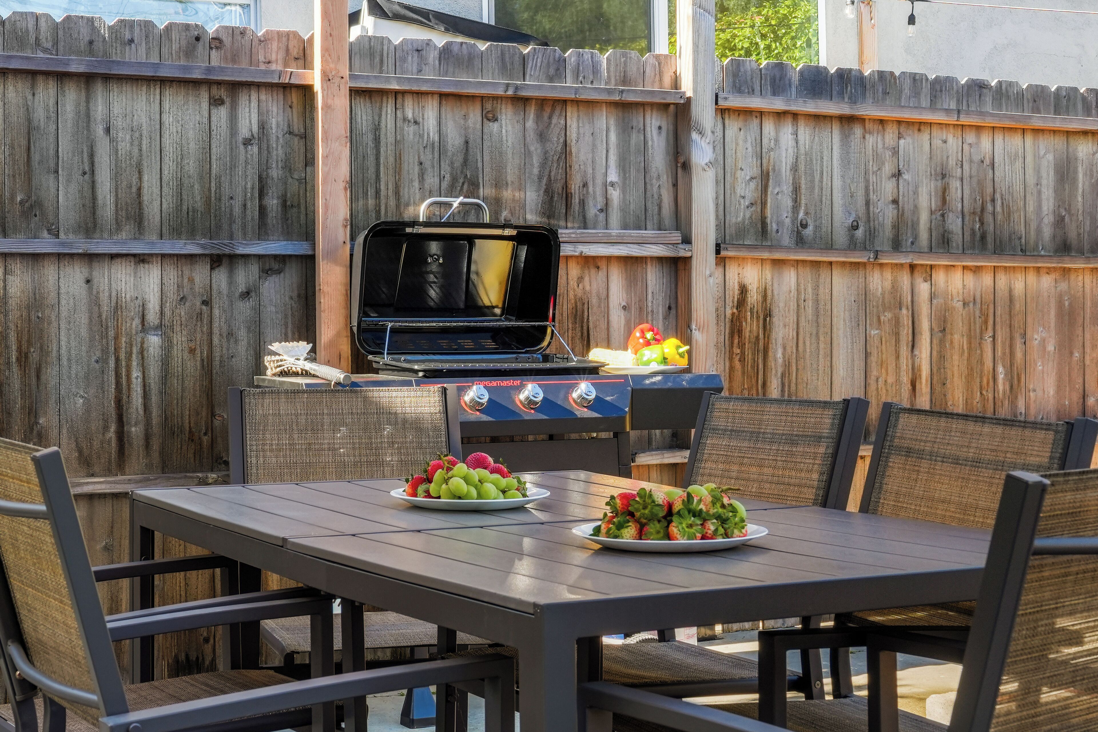 An outdoor patio with a grill, two plates of fruit, and wicker chairs.