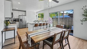 A modern kitchen with white cabinets, a dining area with a wooden table and chairs, and a ceiling fan. - Hot Tub - Firepit - Prime Location - Belmont Shore Retreat - FIFA 2026 (Long Beach)