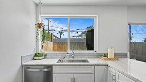 A modern kitchen with a large window, stainless steel appliances, and a wooden fence visible outside. - Hot Tub - Firepit - Prime Location - Belmont Shore Retreat - FIFA 2026 (Long Beach)