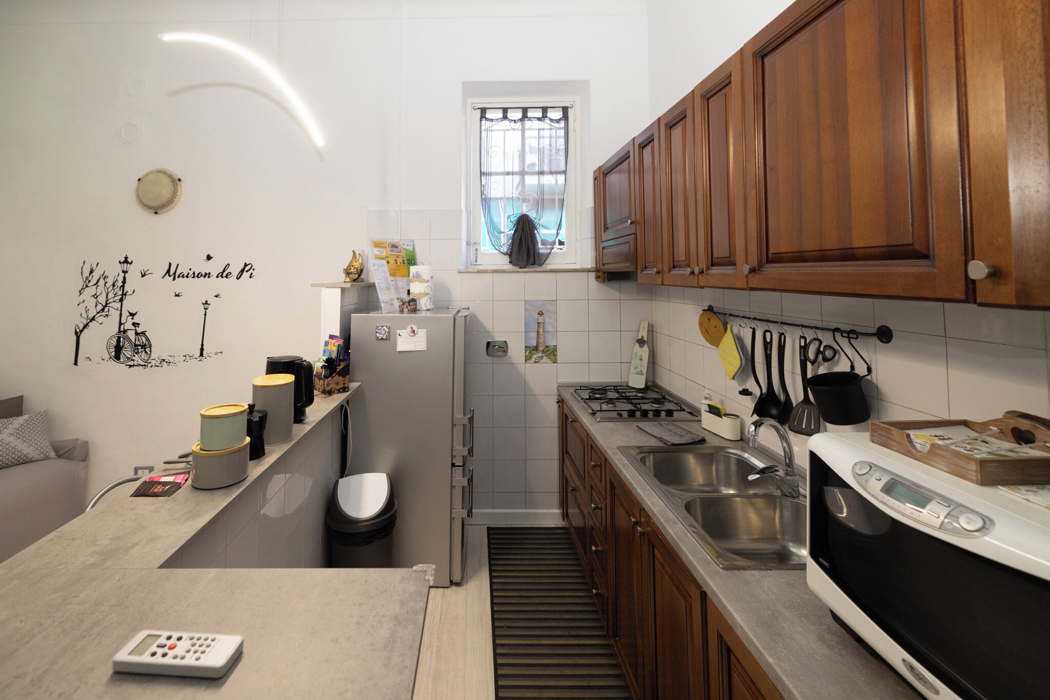 A compact kitchen with wooden cabinets, a built-in oven, a sink, and a window with a curtain.