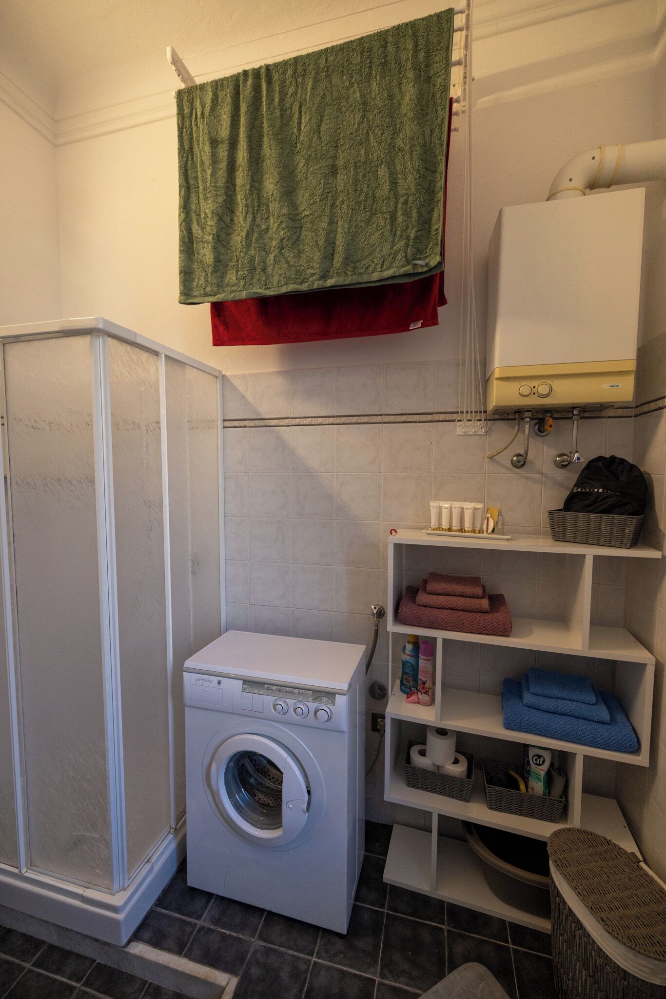 Een wasruimte met een wasmachine, een droogrek en planken met handdoeken en toiletartikelen.