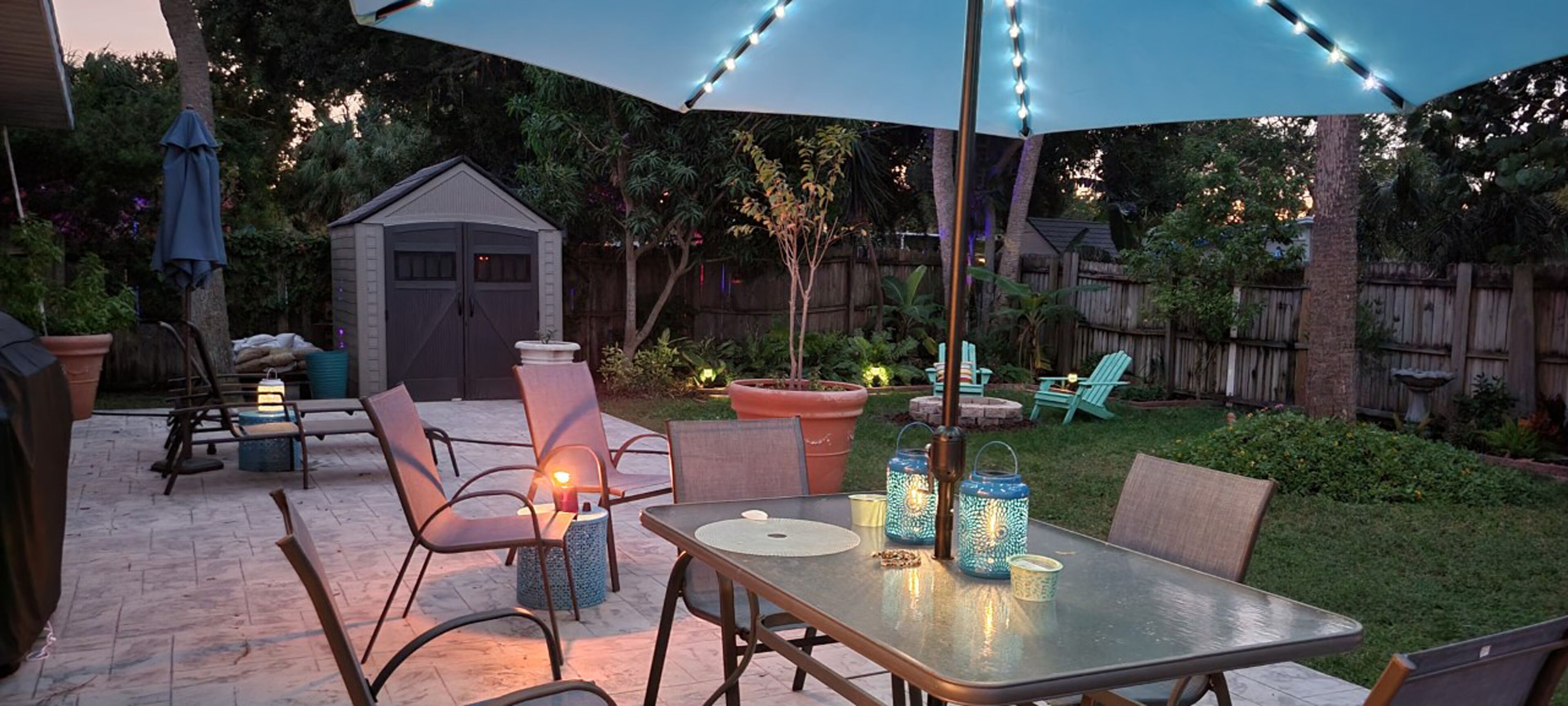 Eine Terrassengruppe im Freien mit Tisch, Stühlen, Lichterkette und einer kleinen Gartenhütte.