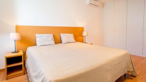 Une chambre à coucher avec un grand lit, deux lampes de chevet, une table de chevet en bois, une armoire et un appareil de climatisation.