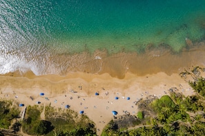 An aerial view of a beach with clear turquoise water, sandy shore, and scattered umbrellas. - Punahoa Beach 201 - Direct Ocean Front, Beautiful Renovation, Split AC, Wi-fi (Kihei)