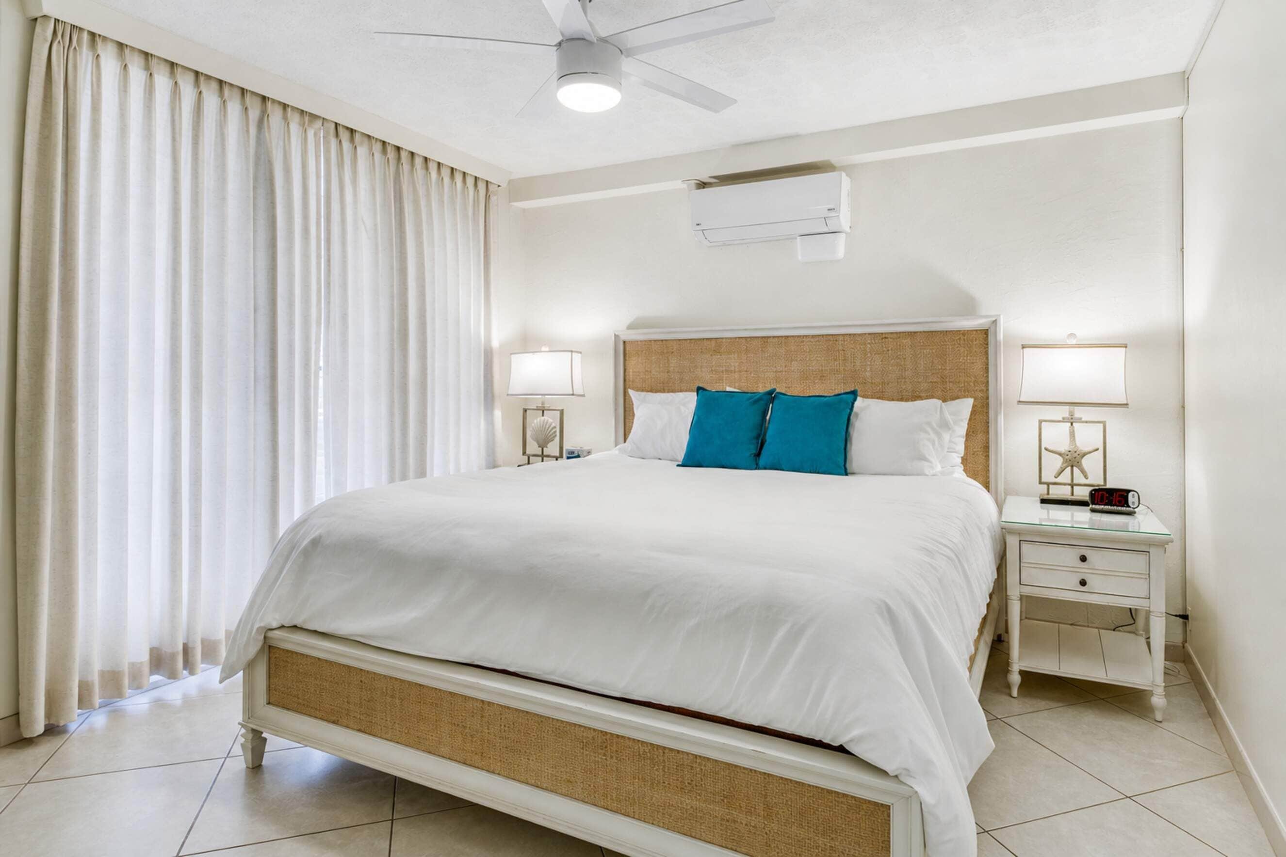 Ein Hotelzimmer mit einem Bett, zwei Nachttischen, einem Deckenventilator, einer Klimaanlage und einem Fenster mit Vorhängen.