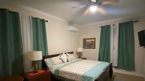 Una camera da letto con un letto, comodini, una lampada, una ventola a soffitto e tende verdi.