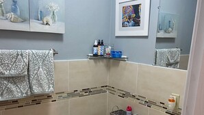Un bagno con il water, un lavandino e uno specchio. Asciugamani appesi al muro e uno scaffale con articoli da toilette.