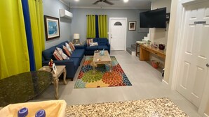 Un soggiorno con un divano blu, un tavolino, una TV e una ventola a soffitto.