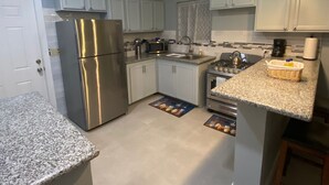 Una cucina moderna con mobili bianchi, elettrodomestici in acciaio inossidabile, piani di lavoro in granito e illuminazione a sospensione.