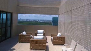 Een balkon met rieten meubilair en een groot raam met uitzicht over de stad.