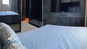 Een moderne hotelkamer met een groot bed, een aan de muur bevestigde televisie en een glazen deur naar de douche.