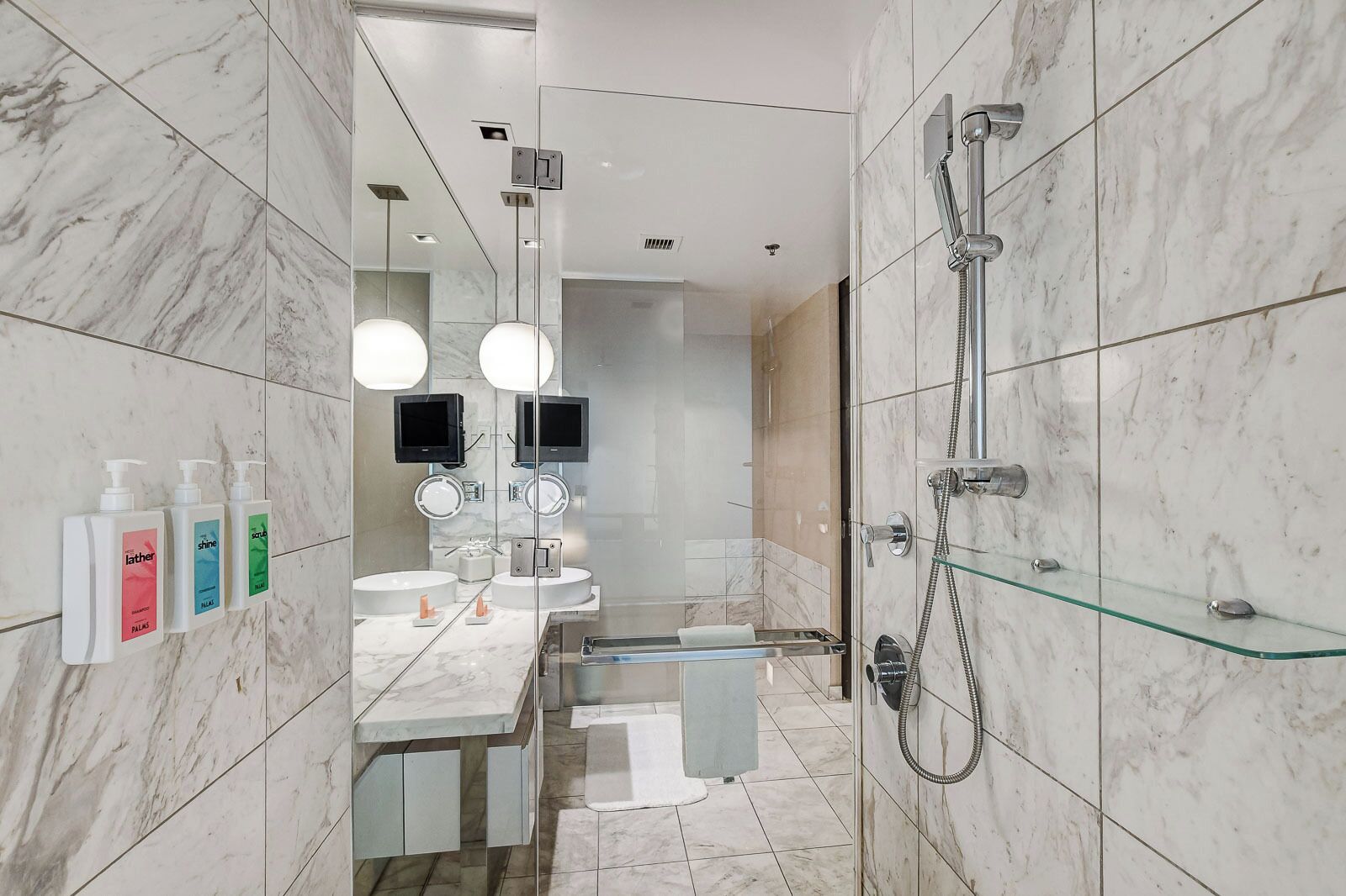 A modern bathroom with marble tiles, a glass shower enclosure, and a vanity with a mirror and two sinks.