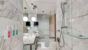 A modern bathroom with marble tiles, a glass shower enclosure, and a vanity with a mirror and two sinks.