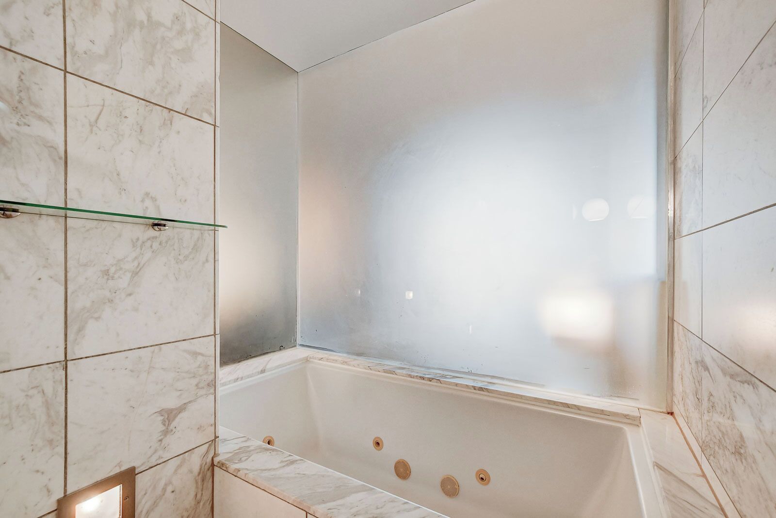 Une salle de bain moderne avec une baignoire sur pieds, des carreaux de marbre et une étagère en verre.