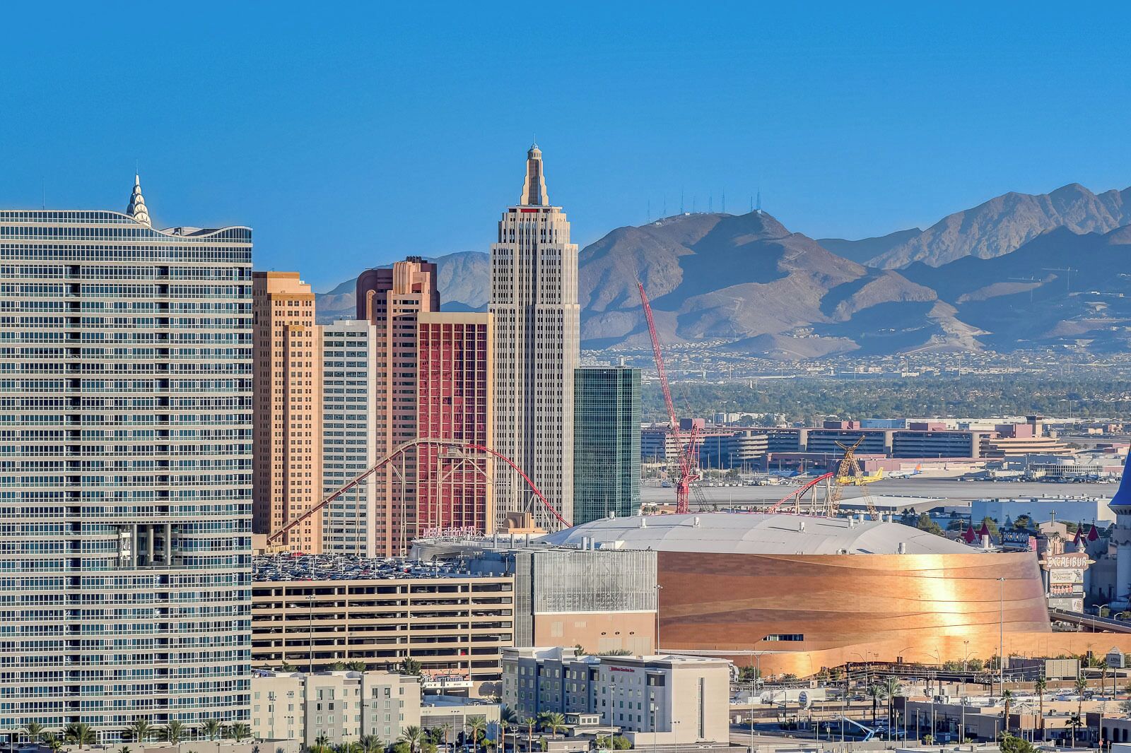 A cityscape with modern high-rise buildings, a large parking structure, and a distinctive curved building with a golden facade.