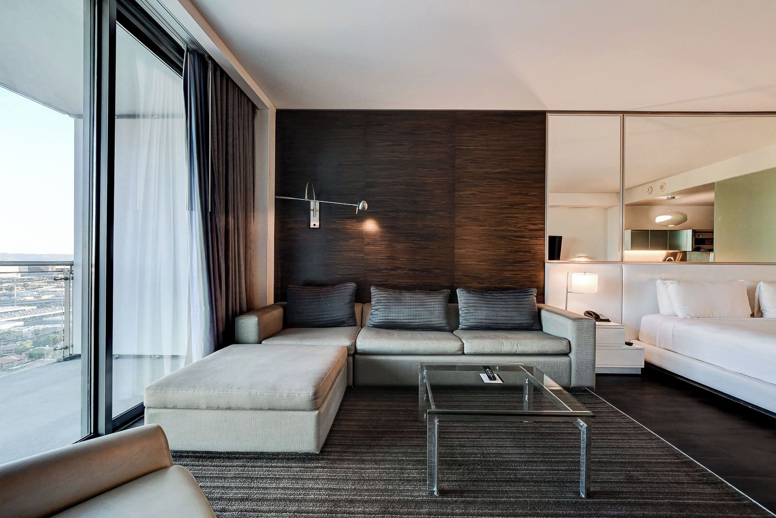A modern living room with a sofa set, a glass coffee table, and a view of the city through large windows.