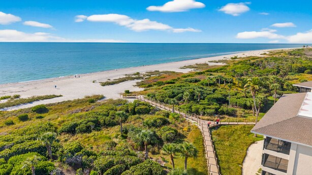 Hotel à beira-mar com vista para a praia, um caminho de paralelepípedos e vegetação exuberante.