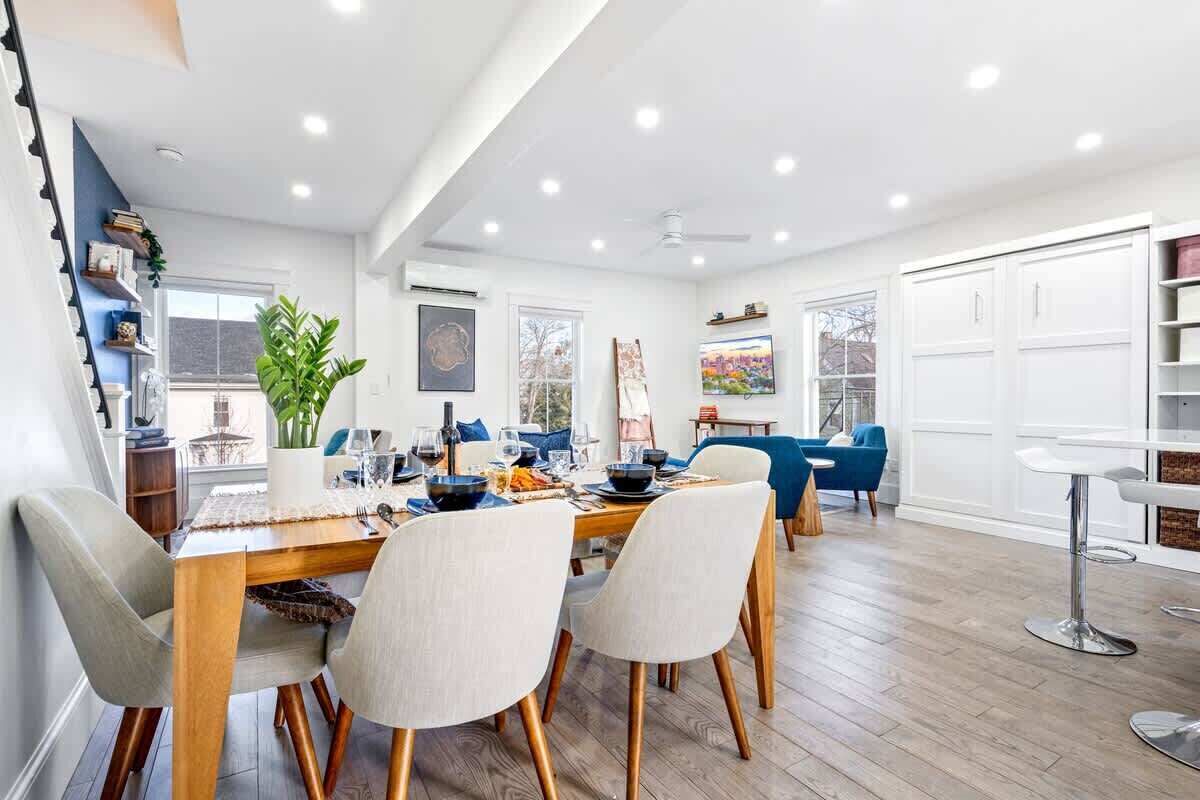 A modern dining area with a wooden table, four chairs, and a bar area with a white countertop and bar stools.