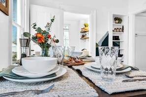 Comedor con una mesa dispuesta para dos, con un tazón blanco, vaso transparente y un jarrón con flores.
