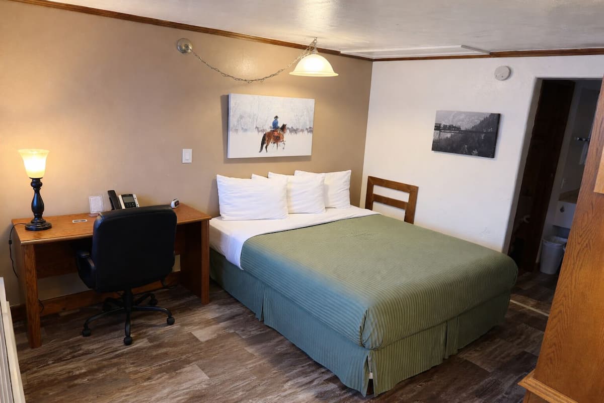 A bedroom with a bed, desk, chair, and two wall-mounted lamps.